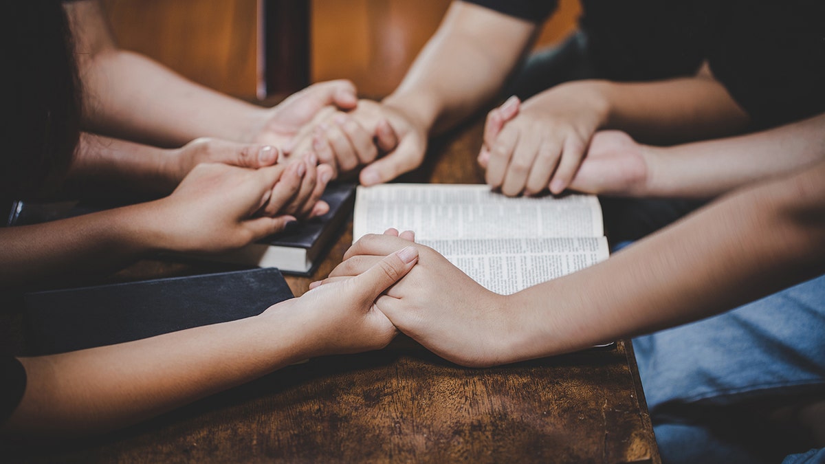 Un grupo de personas orando alrededor de una mesa y sosteniendo biblias.