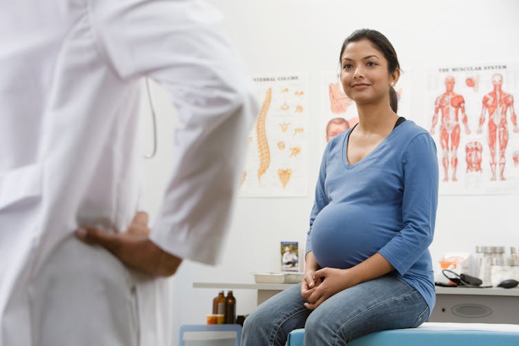 Vista posterior de una mujer embarazada y un miembro del personal médico con una bata blanca en el consultorio de un médico