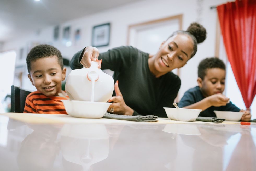 Una madre sentada a la mesa comiendo cereales con sus hijos.
