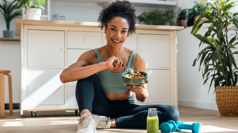 Una mujer sentada en el suelo de la cocina comiendo un plato de comida saludable
