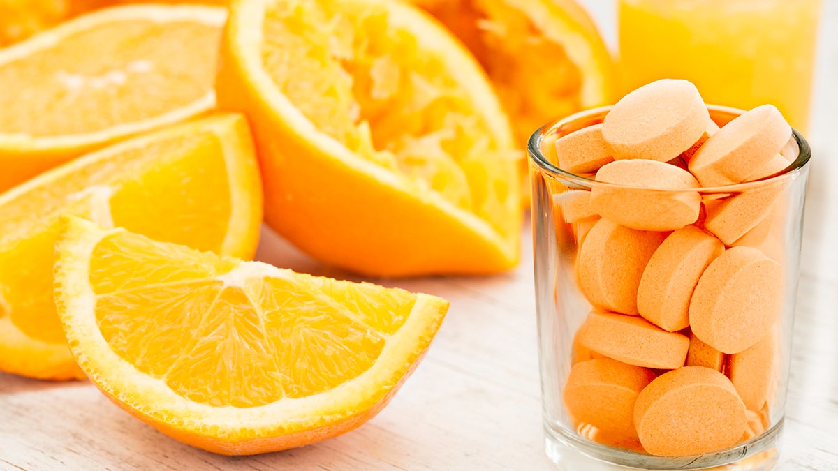 Primer plano de naranja en rodajas y exprimida, un vaso de jugo de naranja y un vaso de pastillas de vitamina C con sabor a naranja