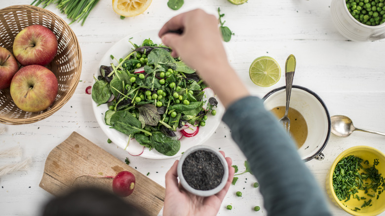 Una mano añadiendo condimentos a un plato de guisantes y verduras.